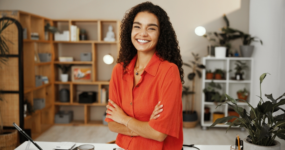 A smiling woman with curly hair and a red shirt stands with arms crossed in an office, Oral Sedation Dentistry at Forest Ridge Dental Health & Wellness