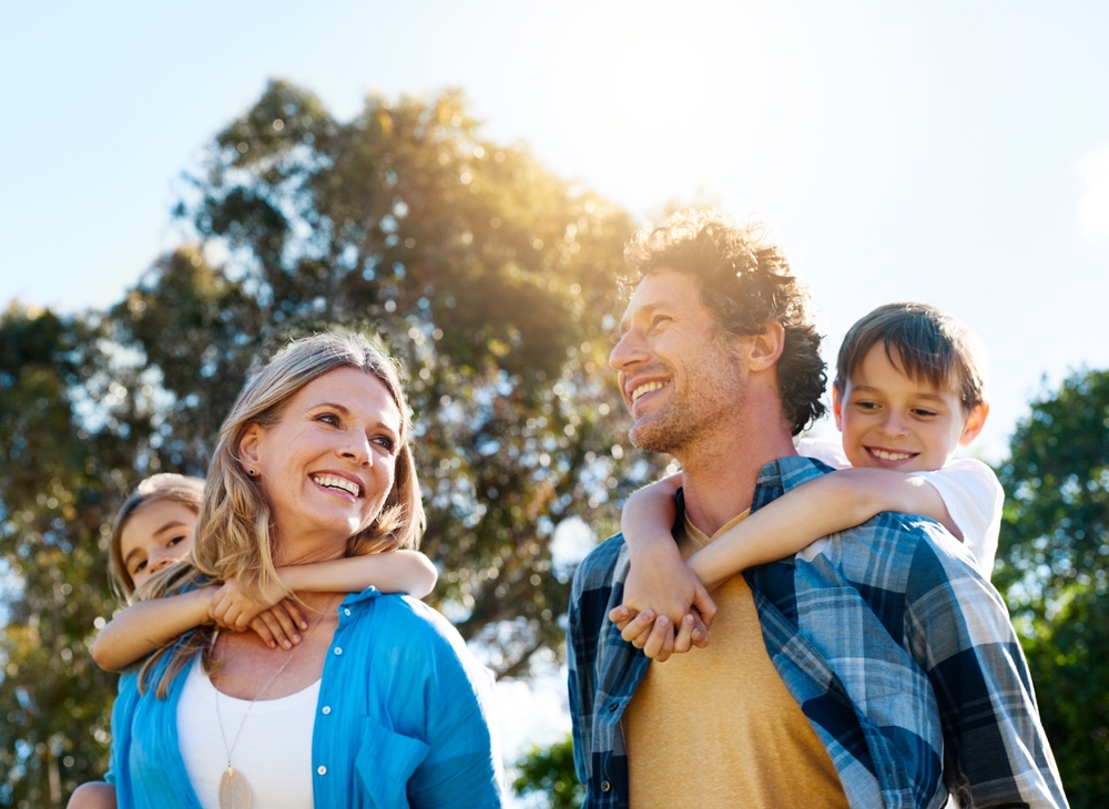 A happy family with children on their parents' backs, enjoying nature, representing Dental Sealants at Forest Ridge Dental Health & Wellness